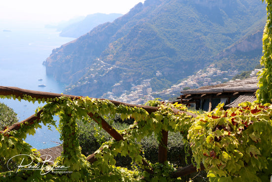 Scenic view from Positano, Italy, overlooking the Amalfi Coast with lush green vines framing the mountains and Mediterranean Sea in the background.