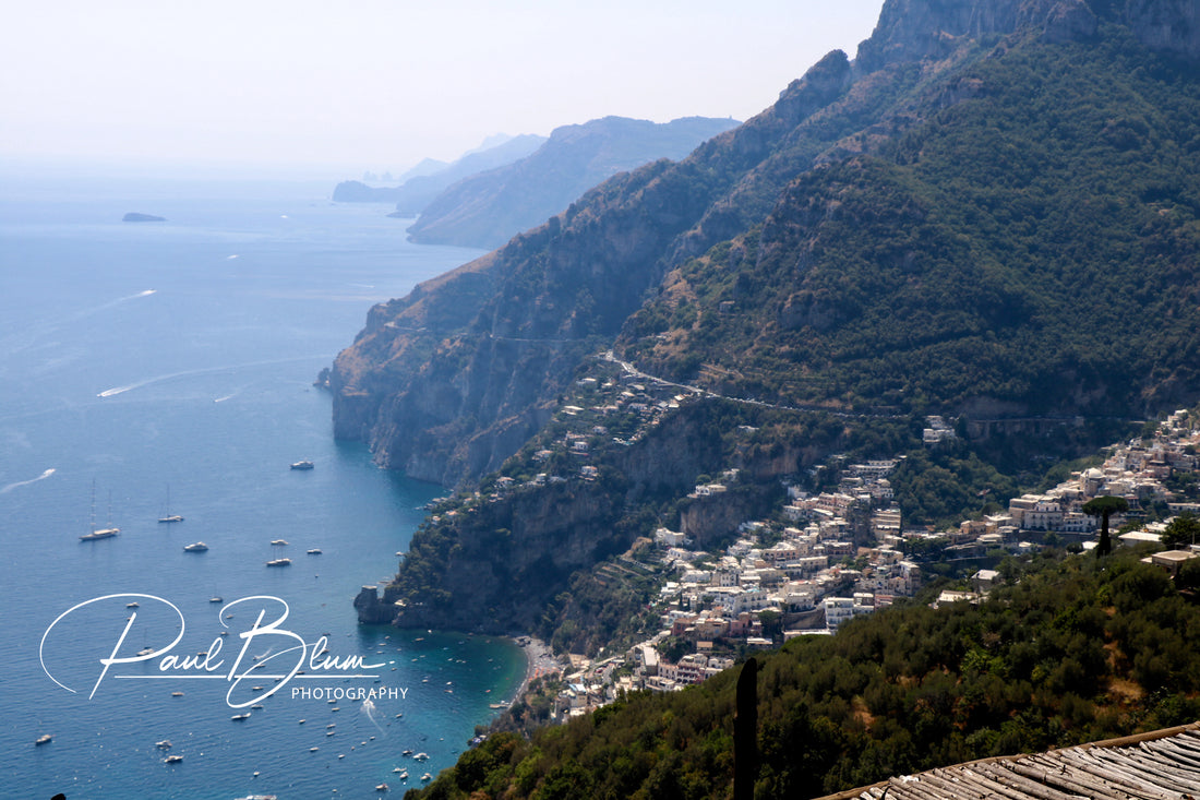 Panoramic view of Positano, Italy, on the Amalfi Coast, with houses cascading down steep cliffs towards the blue Mediterranean Sea, dotted with boats on a sunny day.