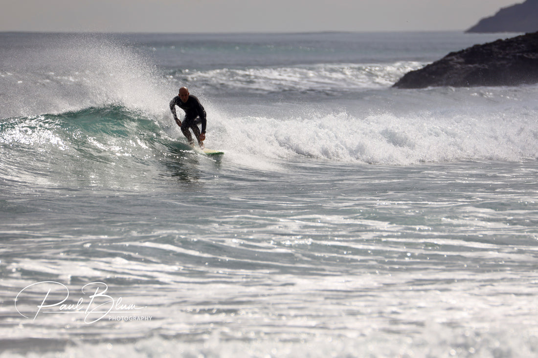 A surfer riding a wave at Piha Beach, captured in action by Paul Blum Photography.