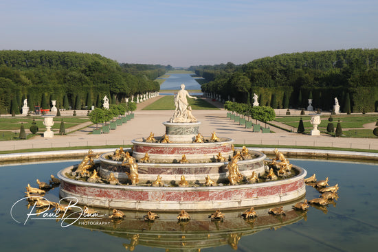 Elegant view of the Latona Fountain at the Palace of Versailles, France, showcasing intricate golden frog sculptures and a central statue, with a grand view of the orderly gardens and reflecting pools stretching into the distance.