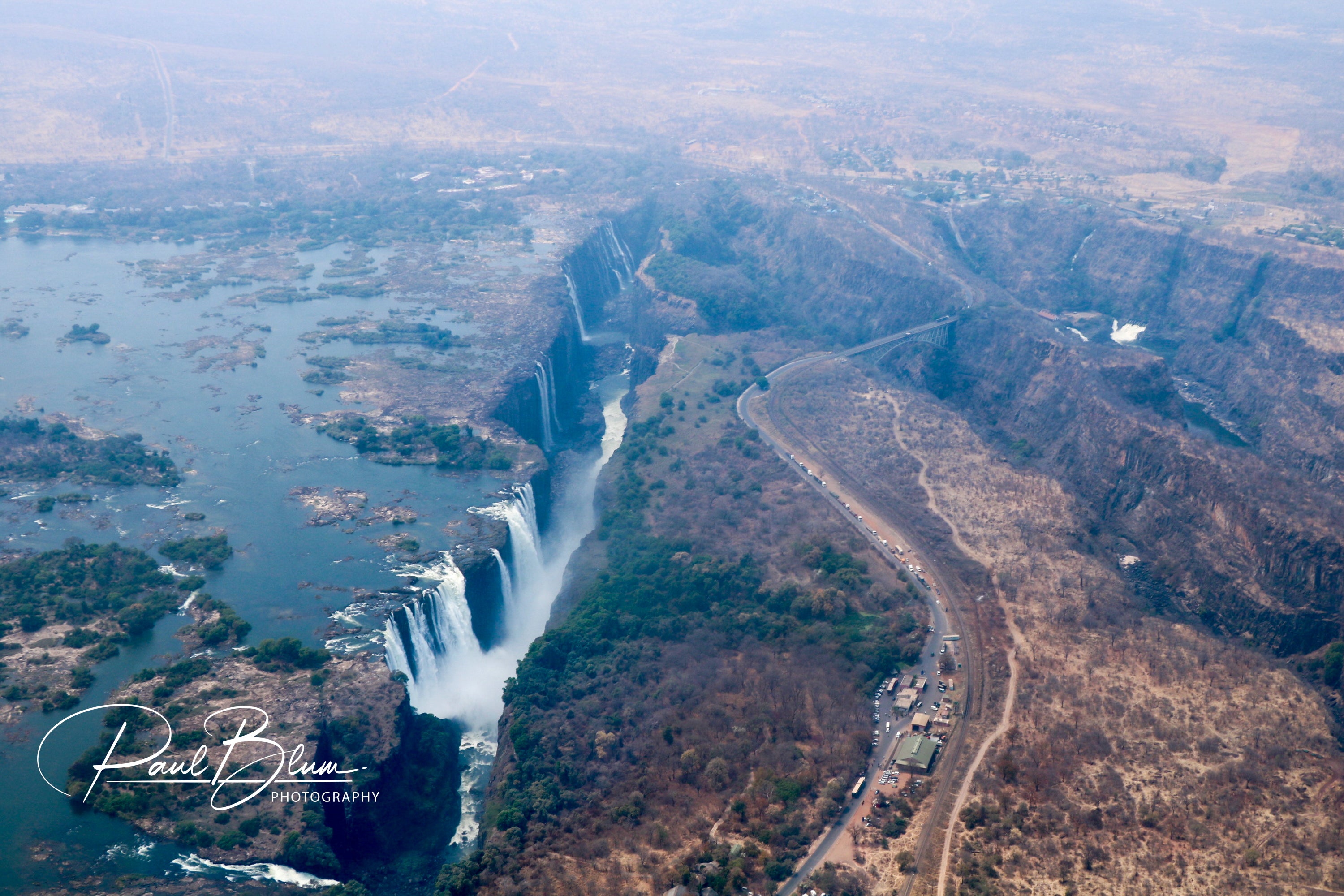 A breathtaking aerial view of Victoria Falls, showcasing the majestic waterfall and surrounding landscape, captured by Paul Blum Photography.